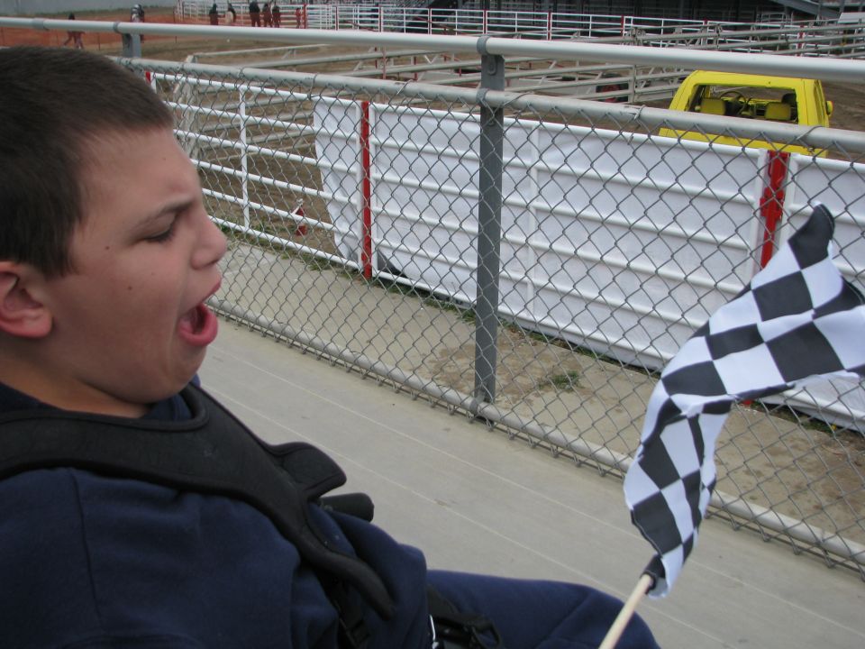 Boy holding a checkered flag by a chain-link fence at a fairgrounds arena