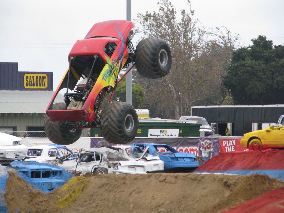Monster truck mid-air over crushed cars, with a saloon building in the background