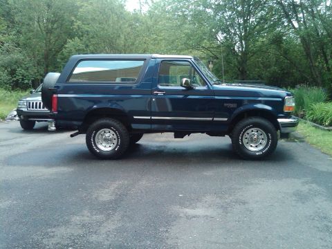 1995 Ford Bronco - Side view of a blue 1995 Ford Bronco parked on asphalt with another vehicle visible behind it.
