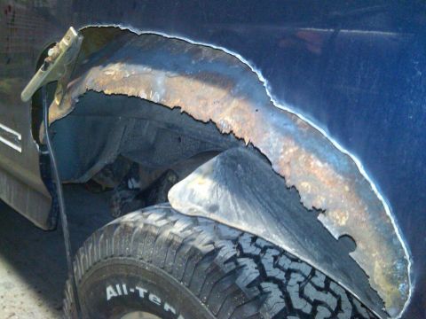1995 Ford Bronco - The wheel well of a vehicle shows significant rust damage and is being prepped for repair.