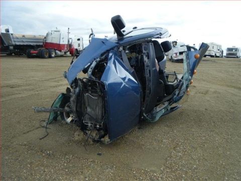 2005 Dodge 3500 - This severely damaged blue vehicle is shown in a field, with other trucks visible in the distance.