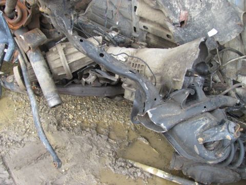 2005 Dodge 3500 - A pile of damaged vehicle parts, including a transmission and suspension components, lies on the ground.