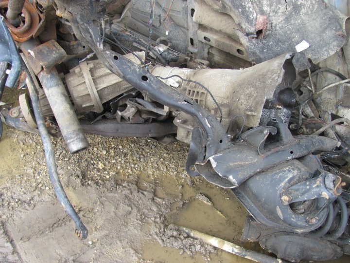 Scrap metal vehicle parts including a transmission and suspension components piled on muddy ground