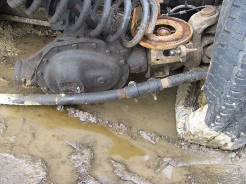 2005 Dodge 3500 - Close-up view of the front axle and suspension system of a vehicle stuck in muddy terrain.