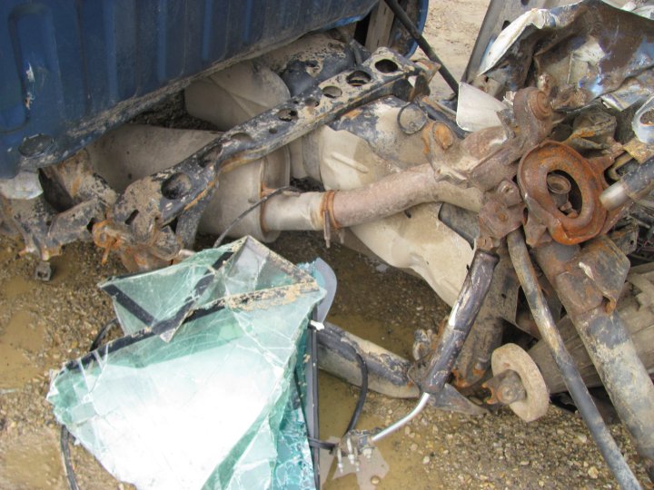 Close-up of a heavily damaged vehicle's undercarriage with broken glass and rusted metal components