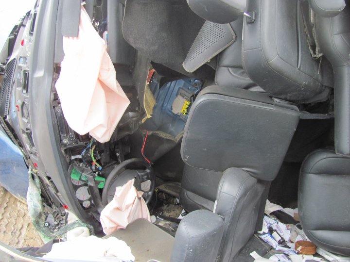 Interior of a damaged vehicle with deployed airbags, torn upholstery, and exposed wiring