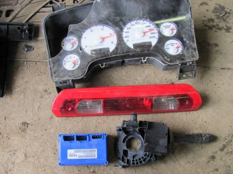2005 Dodge 3500 - Several disassembled vehicle parts are laid out on a concrete surface, including a dashboard instrument cluster and a third brake light.