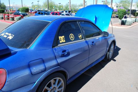 2005 Subaru Impreza - A blue 2005 Subaru Impreza WRX STI is parked with its hood open, displaying custom stickers on the rear window and door.
