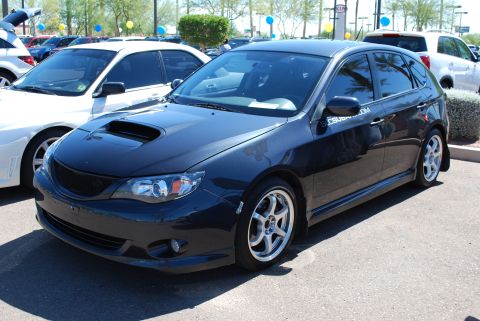 2005 Subaru Impreza - A dark hatchback with a prominent hood scoop is parked at an outdoor event with other vehicles visible.