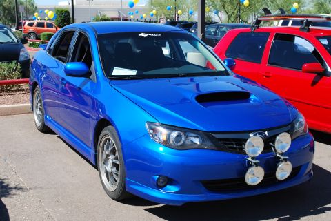2005 Subaru Impreza - A blue 2008 Subaru Impreza WRX STI sedan with rally lights and a hood scoop is parked next to a red car.