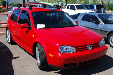 2005 Subaru Impreza - Red Volkswagen Golf Mk4 with surfboards on roof rack, parked next to a silver DeLorean and a white pickup truck.