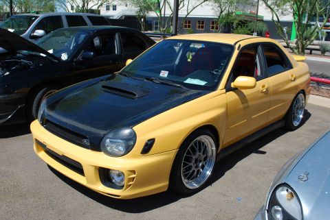 2005 Subaru Impreza - A yellow 2005 Subaru Impreza WRX STI sedan is parked outdoors, a contrasting black carbon fiber hood and custom wheels.