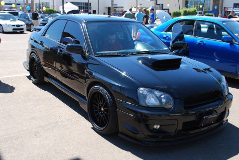 2005 Subaru Impreza - Black 2005 Subaru Impreza WRX STI sedan parked next to a blue Subaru at an auto show.