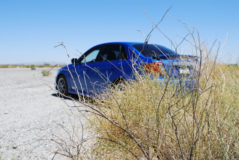 Blue sedan parked on a gravel lot with dry brush in the foreground