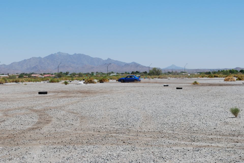 Blue Subaru Impreza drifting on a gravel lot with mountains in the background