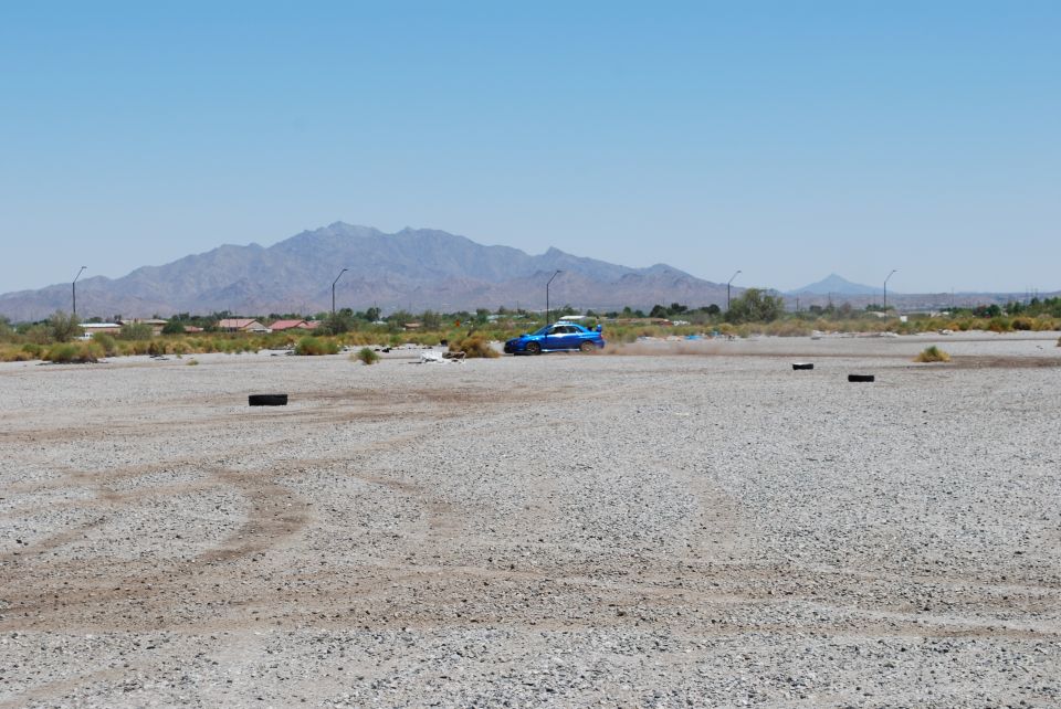 Blue Subaru WRX driving on a gravel lot with mountains in the background