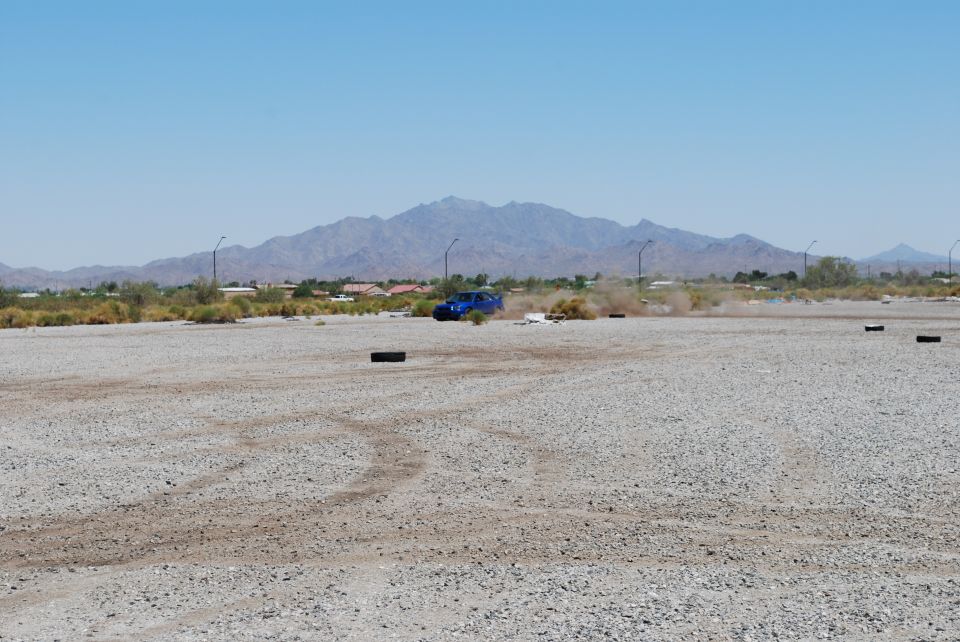 Blue Subaru Impreza kicking up dust on a gravel lot with mountains in the background