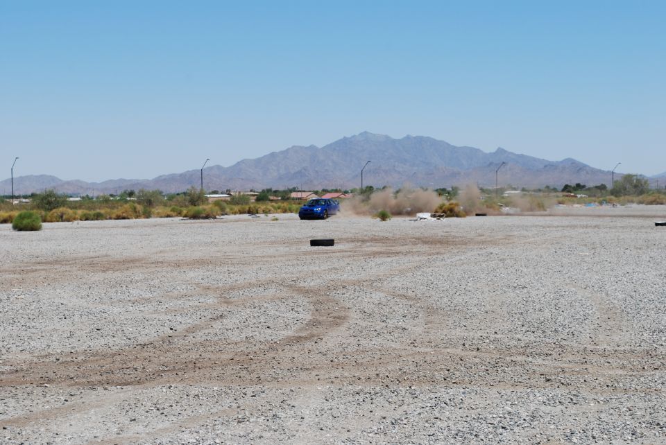 Blue 2005 Subaru Impreza drifting on a gravel lot with dust kicking up