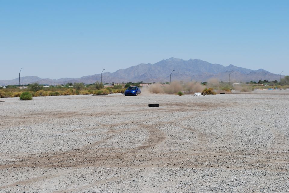 Blue Subaru WRX STI kicking up dust on a gravel lot with mountains in the background