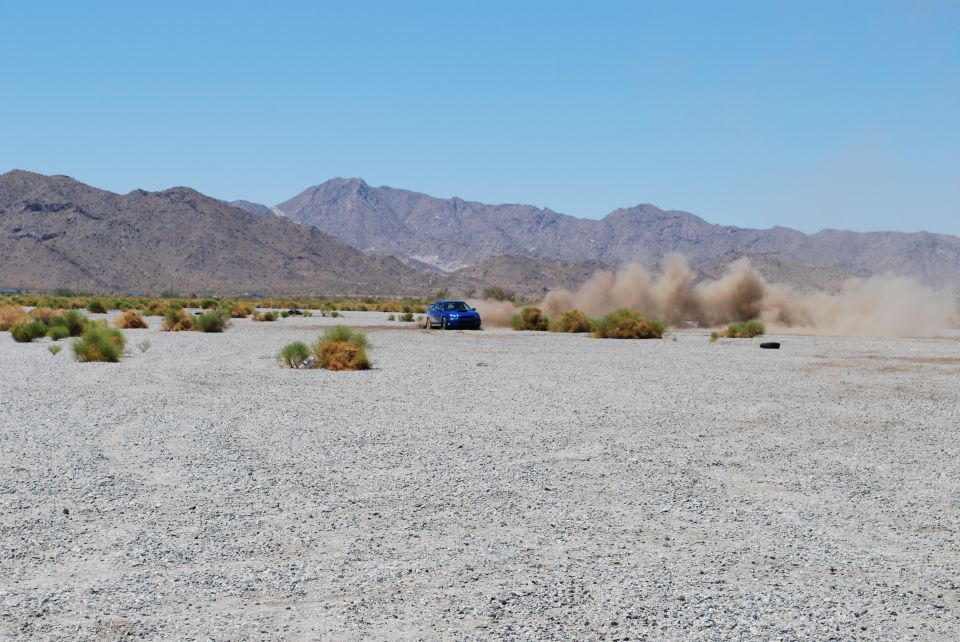 Blue 2005 Subaru Impreza kicking up dust on a desert road with mountains in the background