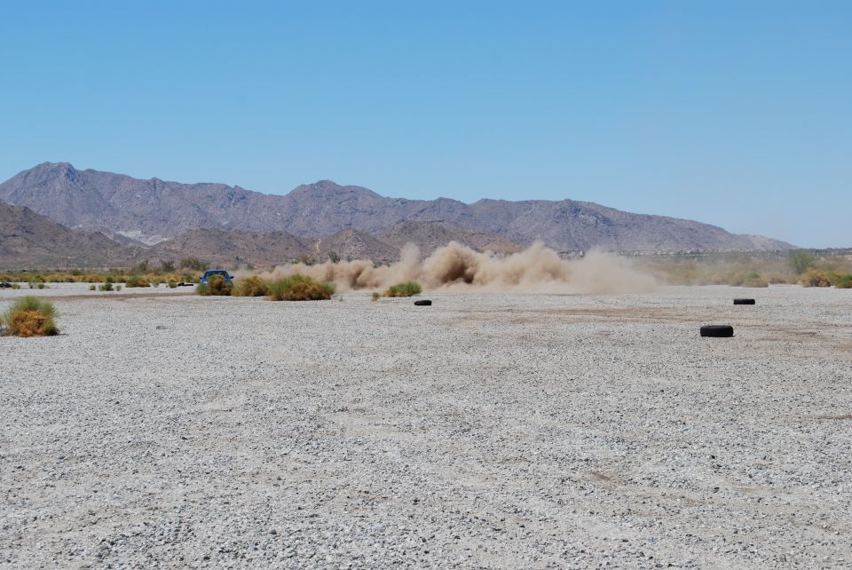 Blue vehicle kicking up a large dust cloud in a desert landscape