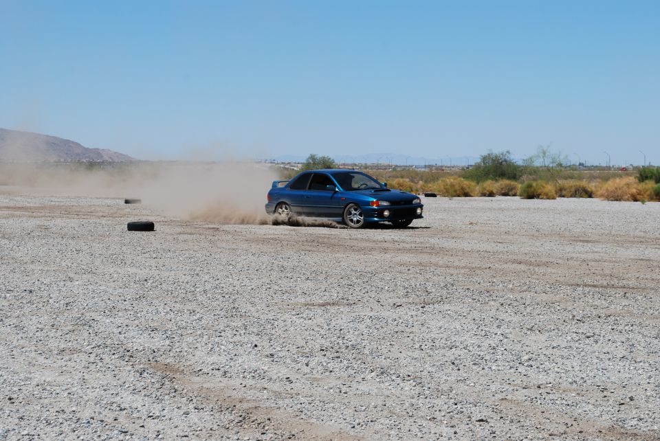 Blue 1998 Subaru Impreza 2-door drifting on a gravel lot, kicking up dust