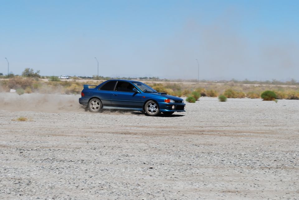 Blue Subaru Impreza drifting on a dirt lot, kicking up dust