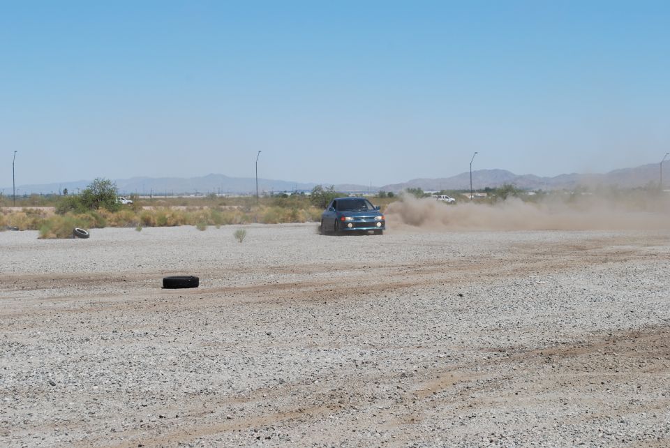 Dark blue sedan drifting on a gravel lot, kicking up dust