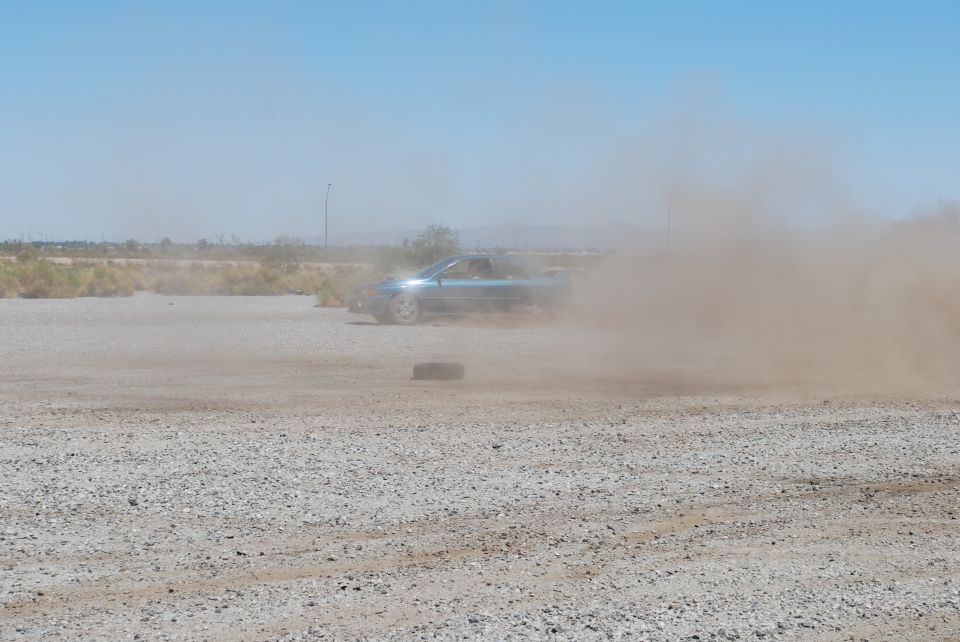 Blue convertible kicking up dust on a gravel road