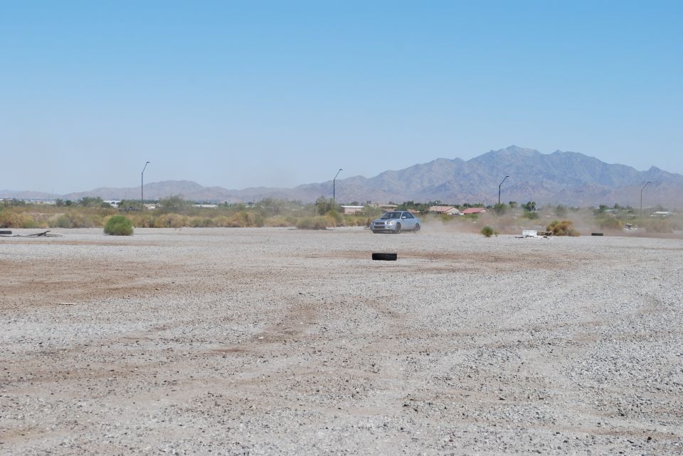 Silver sedan kicking up dust on a dirt road with mountains in the background