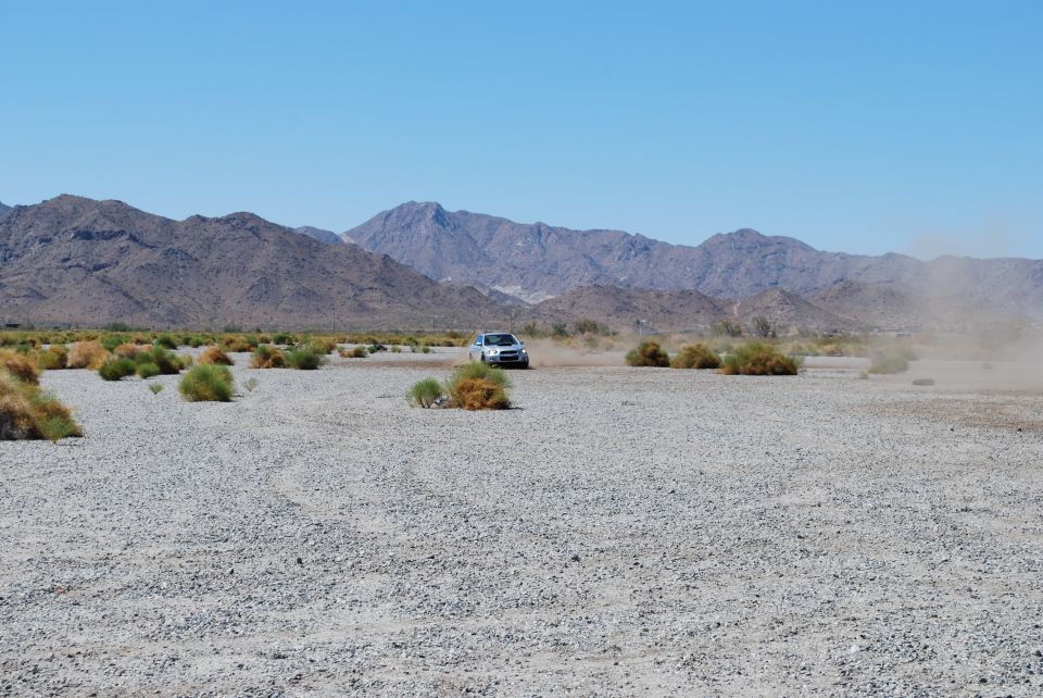Silver sedan driving on a gravelly plain with mountains in the background