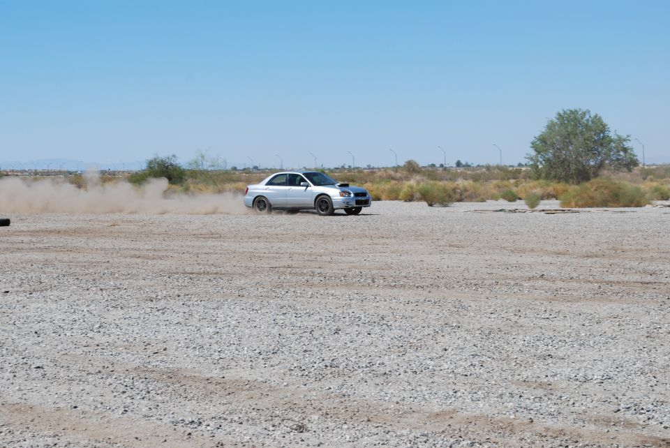 Silver 2005 Subaru Impreza drifting on a gravel lot, kicking up dust