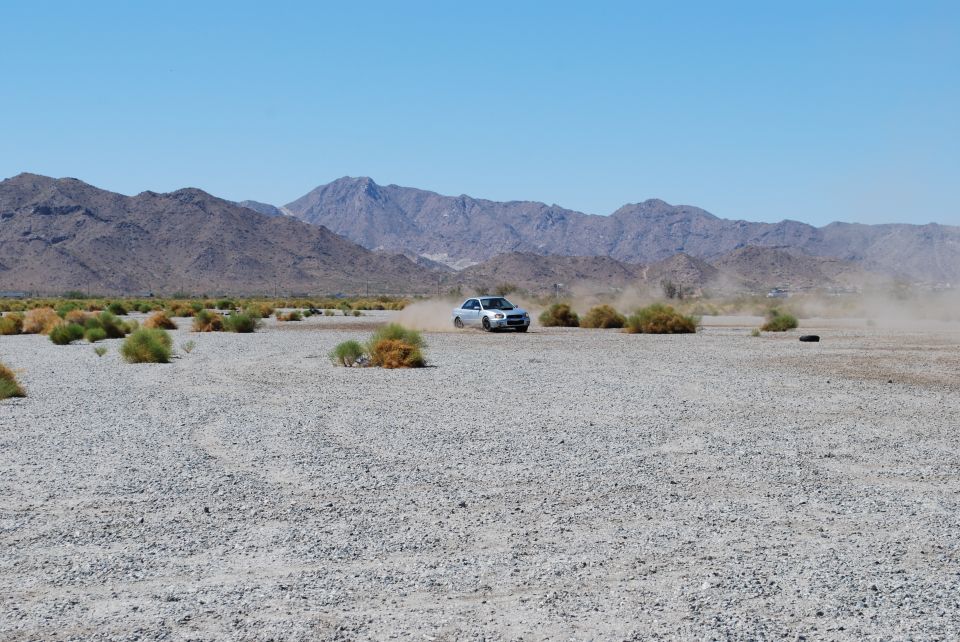 Silver 2005 Subaru Impreza sedan kicking up dust on a dry, gravelly plain with mountains in the background