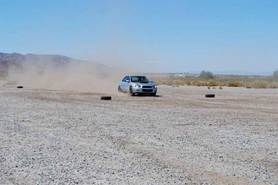 Silver 2005 Subaru Impreza drifting on a dusty gravel track with tires marking the course