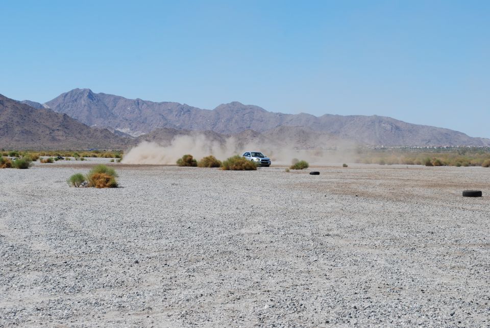 Silver SUV driving on a dusty, gravelly plain with mountains in the background