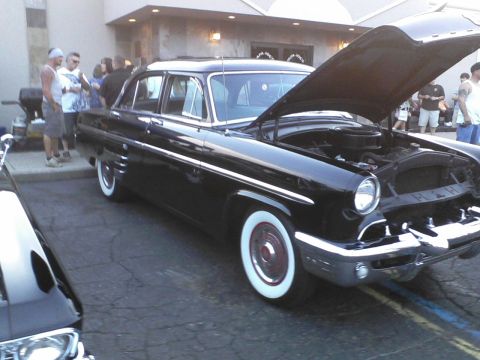 1960 Ford Falcon - Black 1954 Mercury sedan with whitewall tires and hood open, parked outdoors with people around.