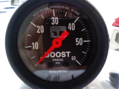 1990 Ford Bronco - Extreme close-up of a new Auto Meter mechanical boost pressure gauge, black face marked 0-60 PSI with a red pointer resting at zero and "Au…