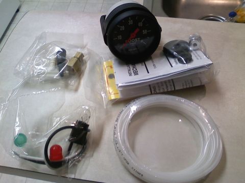 1990 Ford Bronco - A boost gauge and its associated installation components are laid out on a countertop.