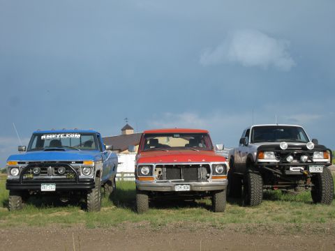 1978 Ford Bronco - Three trucks, a blue Ford, a red Ford, and a silver Ford Ranger, are lined up in a grassy field.