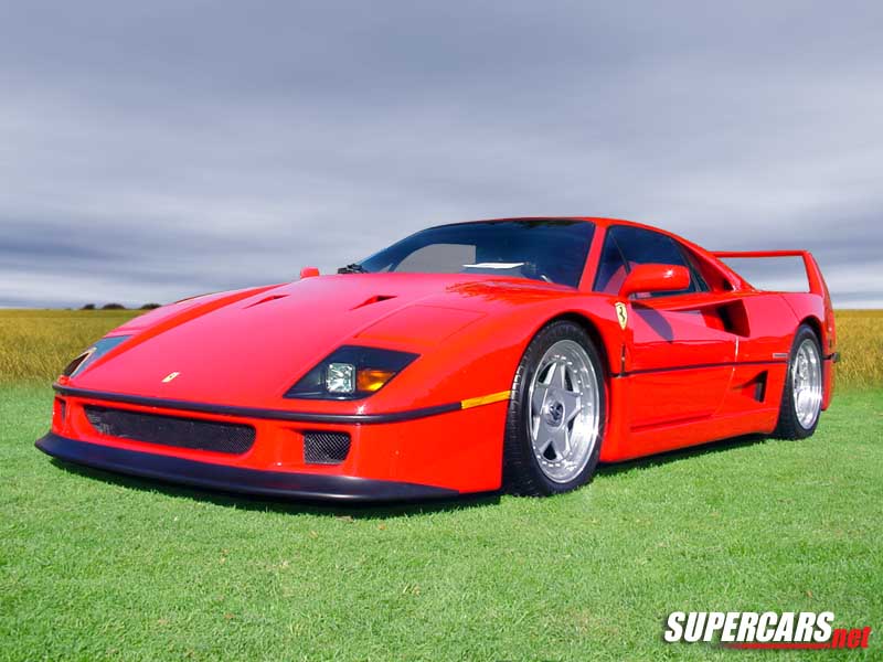 Red sports car with a large rear wing parked on grass