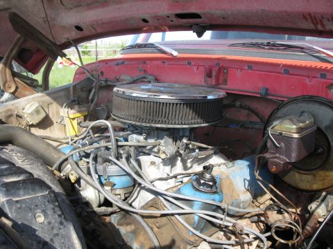 1978 Ford Bronco - The engine bay of a red 1978 Ford Bronco is visible, showing the carburetor and air filter assembly.