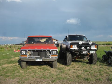 1978 Ford Bronco - Two pickup trucks are parked side-by-side in a grassy field under a cloudy sky.