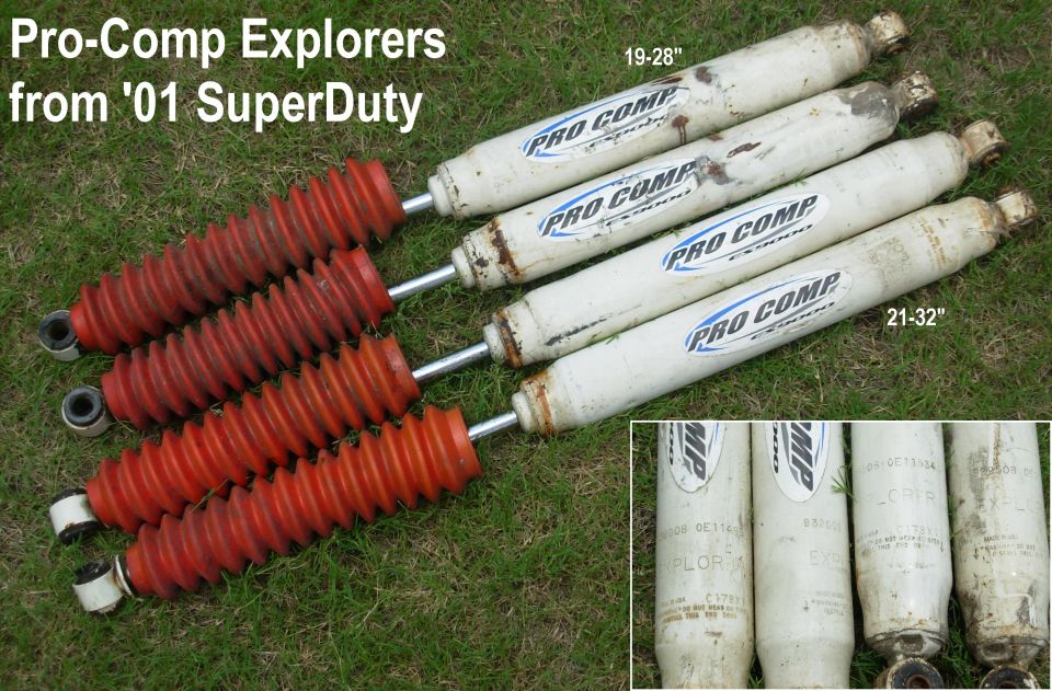 Four Pro Comp shock absorbers with red boots from 2001 Super Duty laid on grass