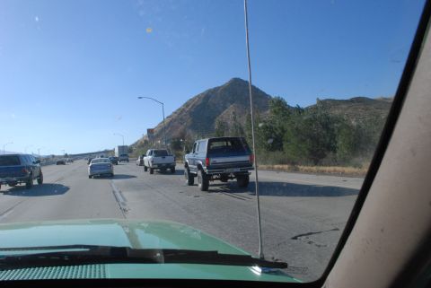 1996 Ford Bronco - A blue Ford Bronco is seen from behind on a highway, with other vehicles around it.