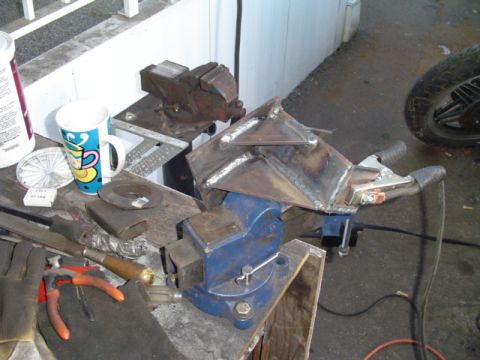 1993 Ford Bronco - A custom metal bracket is being worked on in a vise, with various tools and a mug nearby.