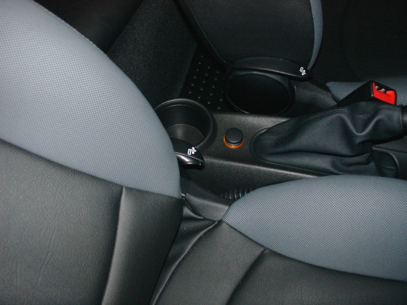 Car interior showing black and grey seats, a gear shifter, cup holders, and a red seatbelt buckle