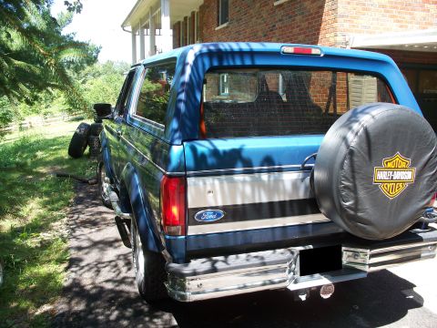 1995 Ford Bronco - The rear of a blue 1995 Ford Bronco is visible, a spare tire cover with the Harley-Davidson Cycles logo.