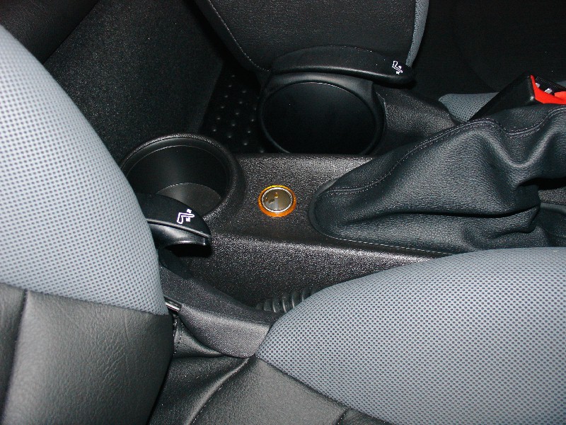 Car interior showing a cup holder, a 12v power outlet, and a leather-wrapped gear shift boot