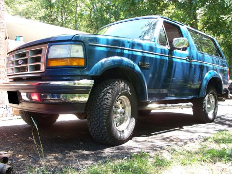 1995 Ford Bronco - This blue Ford Bronco is parked on a gravel driveway with trees in the background.