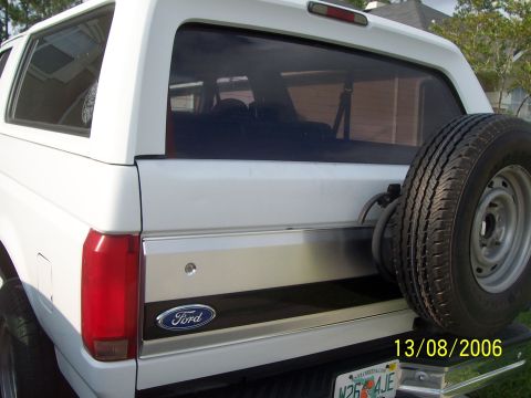 1994 Ford Bronco - Close rear three-quarter view of a white full-size Ford Bronco's tailgate and liftglass, showing the brushed-aluminum tailgate applique wit…